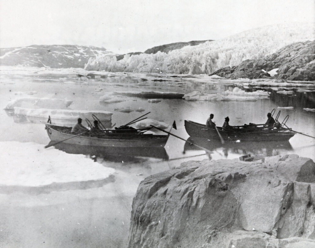To småbåter med to og tre personer i en fjord med stor brefront i bakgrunnen