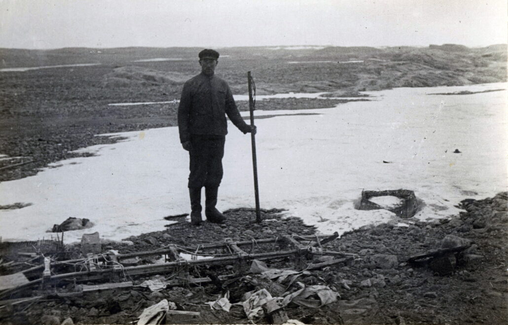 En mann står ved funnet av restene av leiren. Han holder en stokk i venstre hånd
