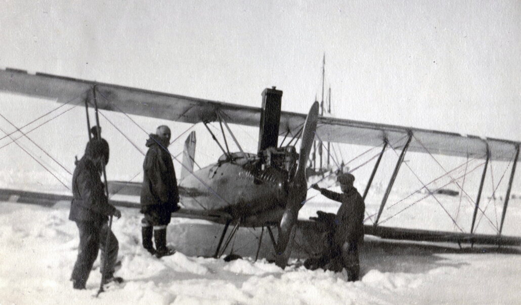 Tre personer står ved et lite propellfly stom står på snedekket bakke