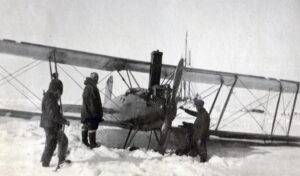 Tre personer står ved et lite propellfly stom står på snedekket bakke