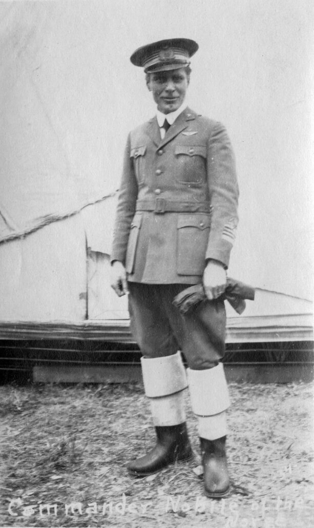 Mann i uniform med støvler på bena og handkser i ene hånda
