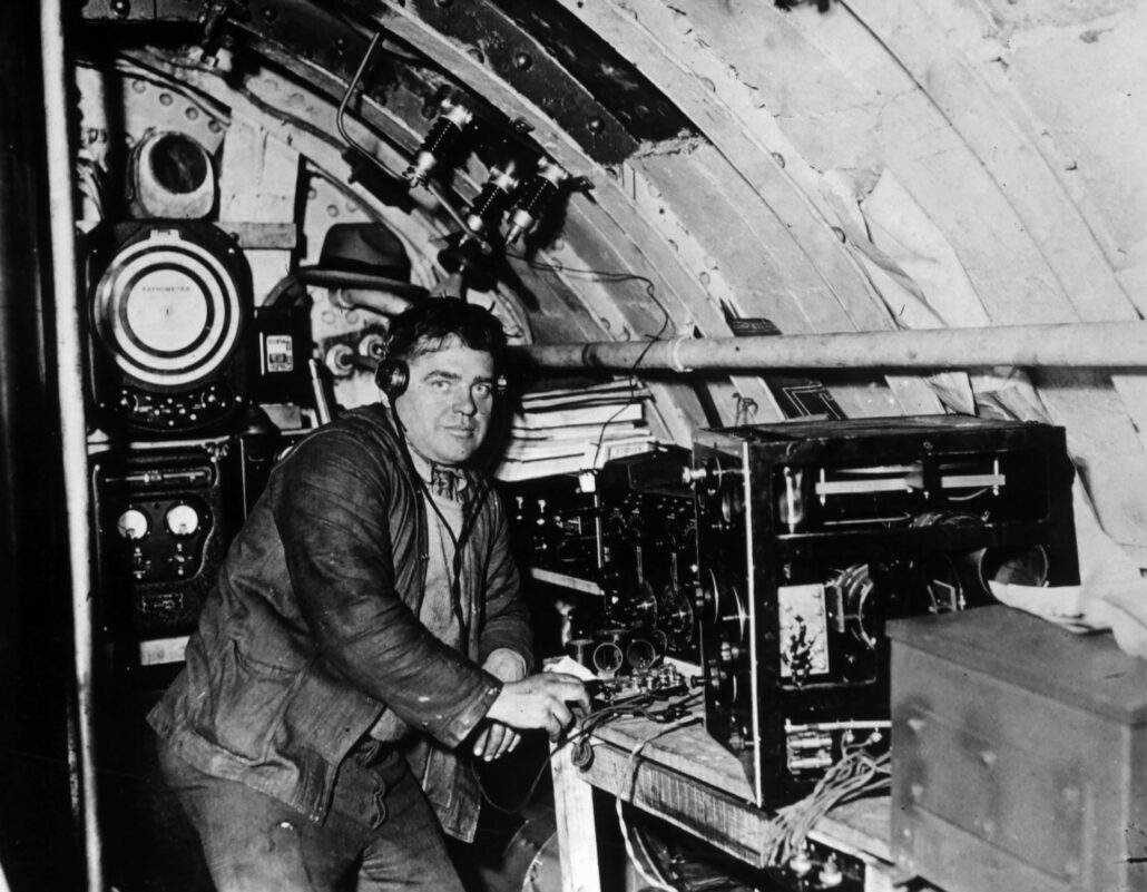 Mann står ved radio i ubåt, masse radioutstyr bak han.