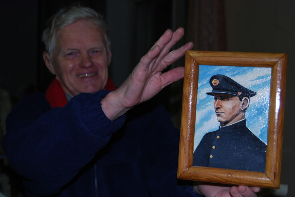 Mann smiler og holder frem et portrett av mann i uniform