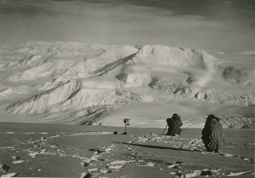 Snedekte fjell og to personer som sitter på huk og tar bilder