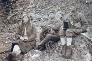 En kvinne og to menn sitter i en steinur med apparater på fanget. Kvinnen har skjørt.
