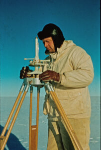 Mann med hvit anorakk og sort lue gjør målinger med en apparat på tre føtter