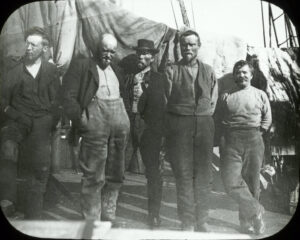 Fem skjeggete menn står på båtdekk, ullklær og en har pipe