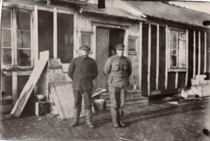 To menn står foran en enkel bygning i tre