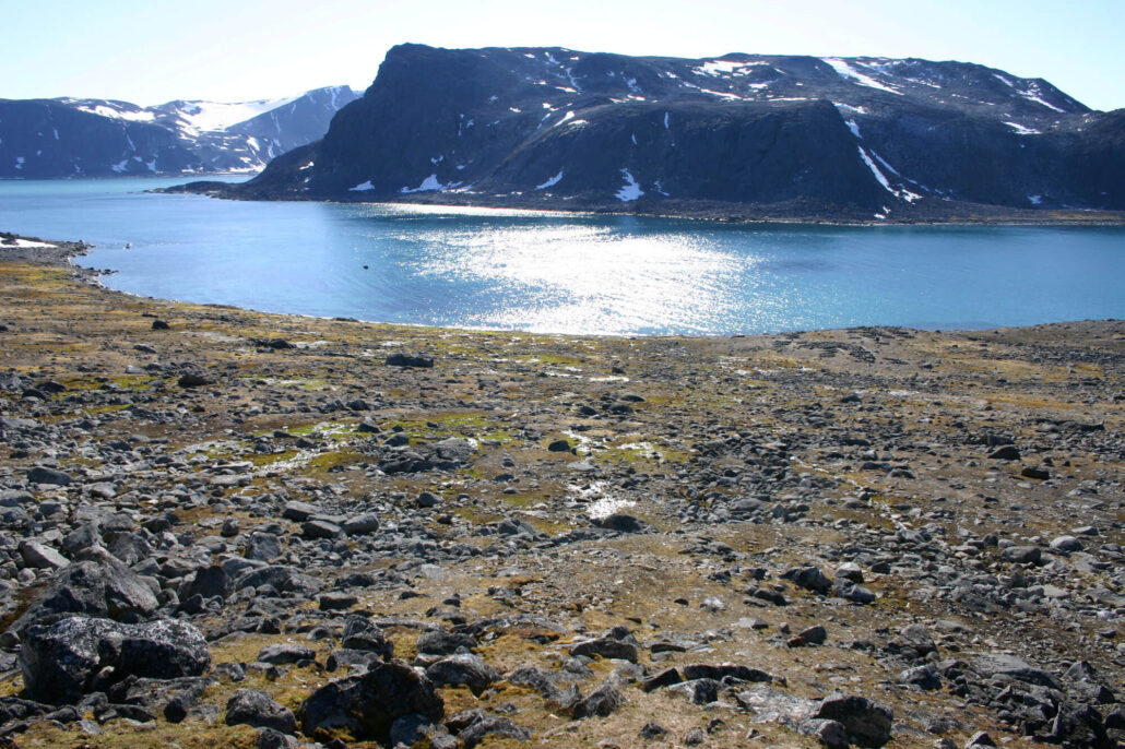 landskapsbilde med stein på terreng, hav og fjell i bakgrunnen