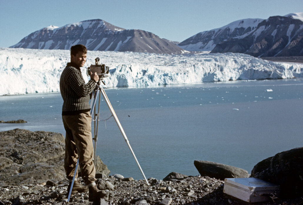 mann står ved isbre med et apparat på en tripod
