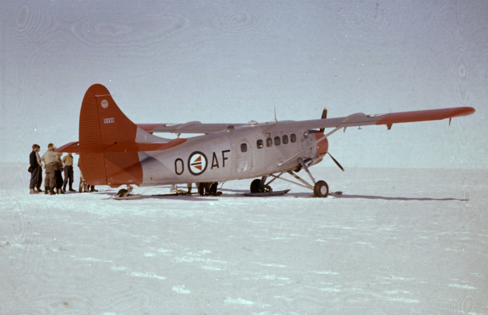 Et lite fly står på snedekekt bakke, en gruppe personer står bak til venstre