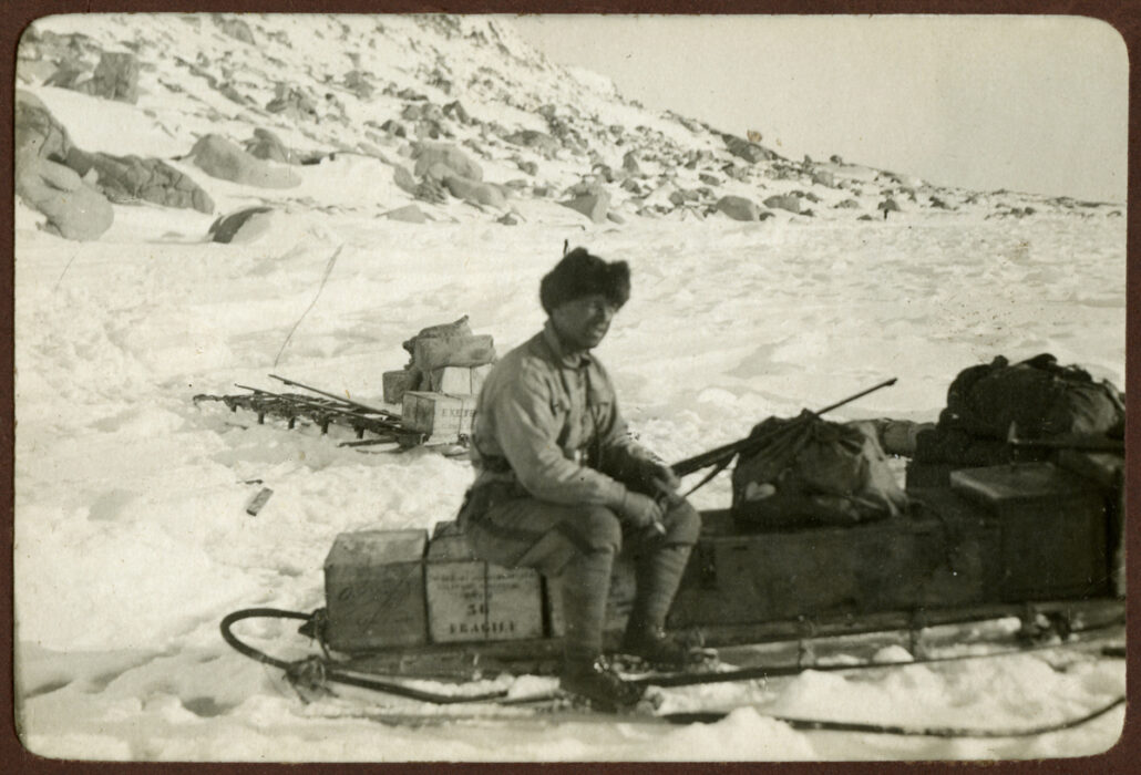 Man sitter på en kasse på en slede med et gevær i hendene
