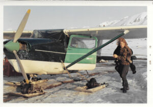 Kvinne står ved siden av et lite propellfly. Hun har rødlig hår og pelsjakke