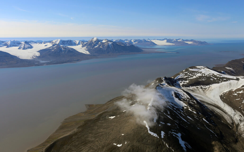 flyfoto bilde av fjord. Snødekkede fjell ligger på begge sider.