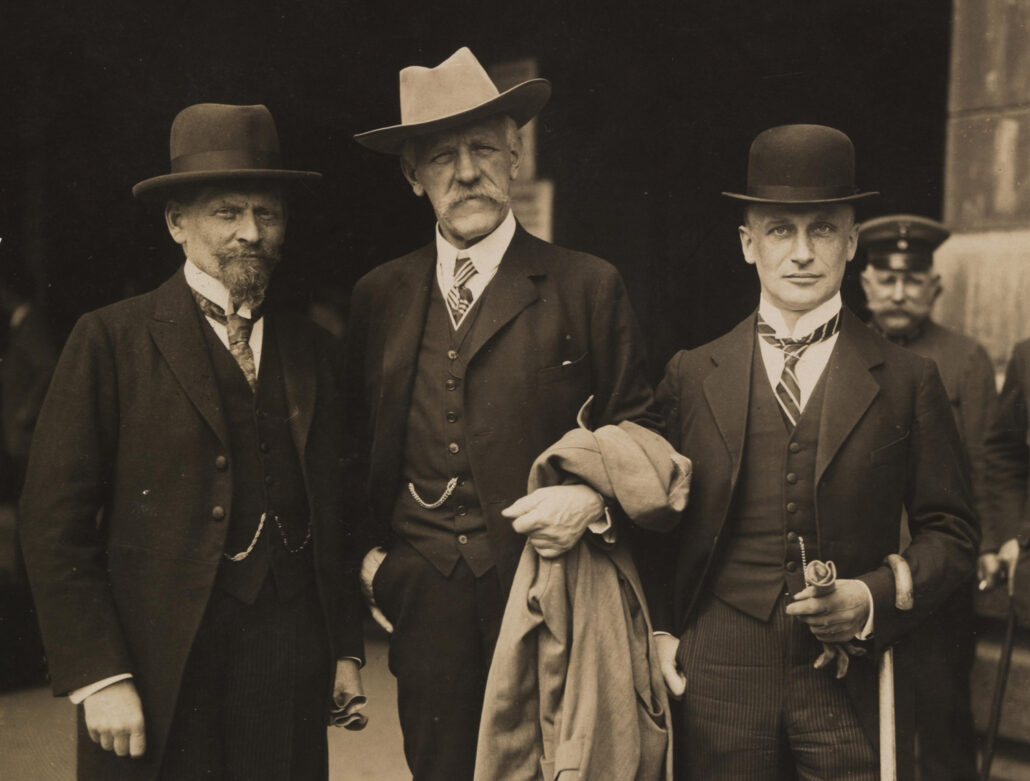 Tre menn poserer i med frakk og hatt