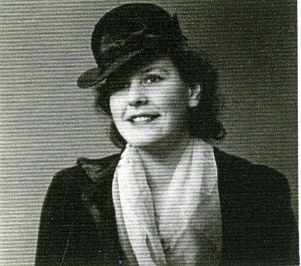 Portrett av kvinne med sort hatt og jakke, samt hvitt løst skjerf hengende rundt halsen