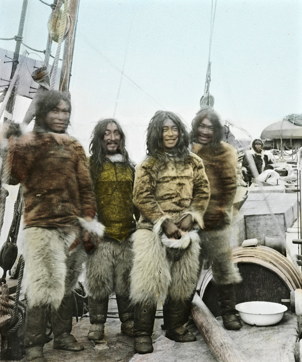 Fire smilende inuitter i pelsklær og halvlangt hår ombord på en skute