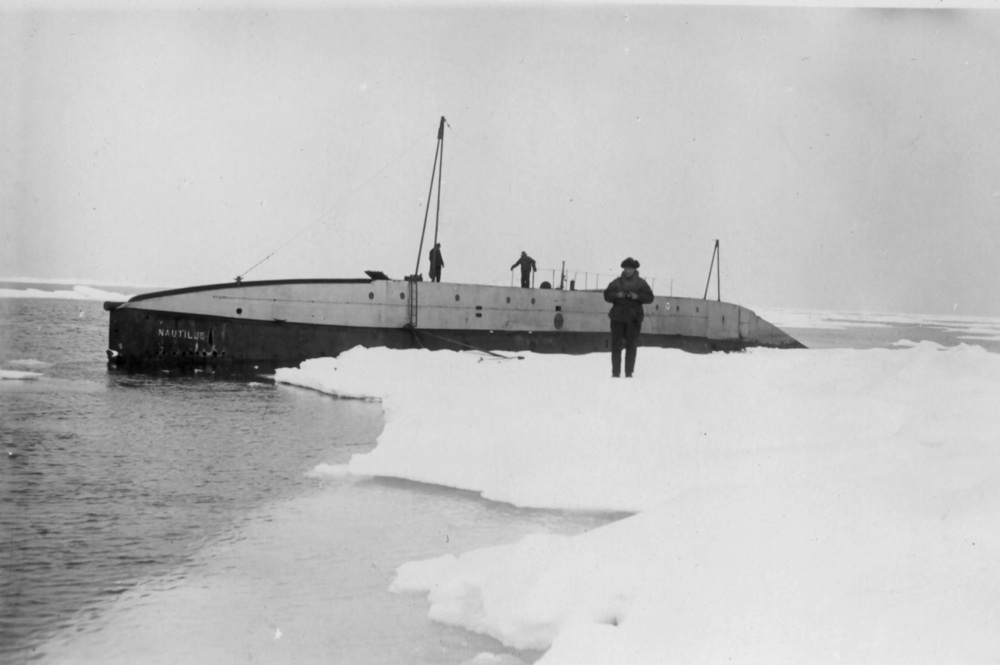Ubåt ligger ved en iskant. To personer står på ubåten og arbeider. En mann står foran