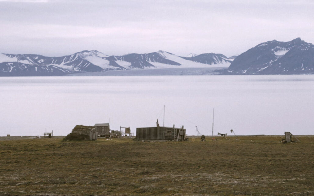 Små trebygninger i rfogrunnen, hav og fjell i bakgrunnen